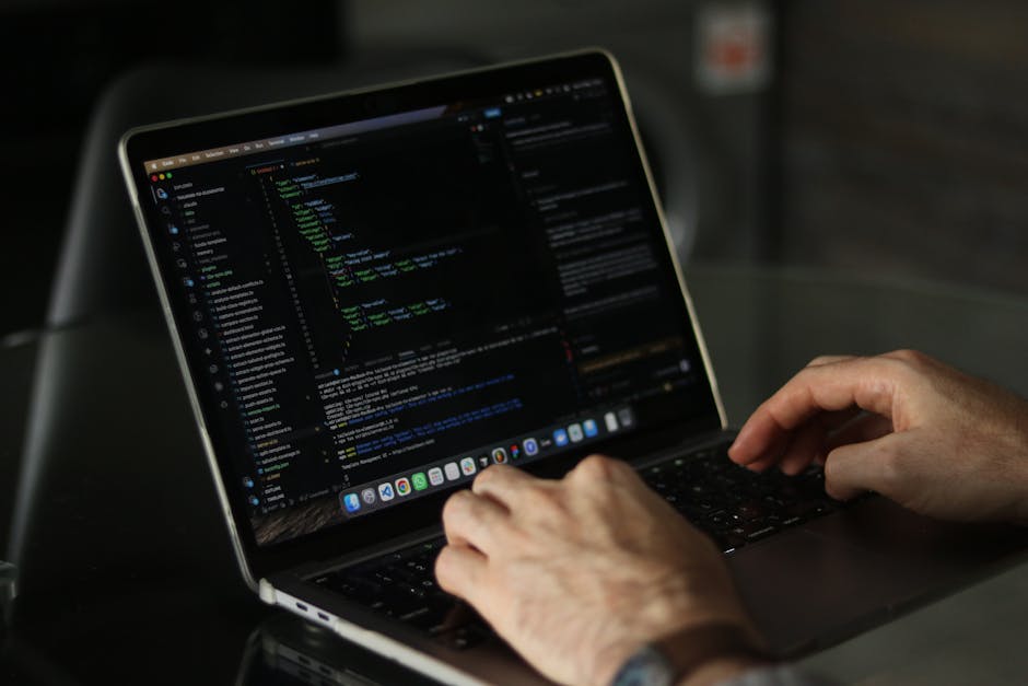 A person working on a laptop with a dark screen displaying lines of colorful code, possibly related to gardening or landscaping software. The individual is seated at a table, with their hands typing o
